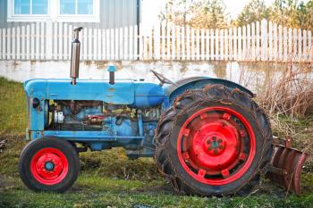 Small old blue tractor with red wheels stands on grass nearby wooden fence in Norway