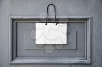 Empty white plate for information text hanging on gray wooden door