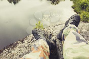 Male feet in camouflage pants and black rough shoes, travel background. Vintage tonal correction photo filter, old style effect