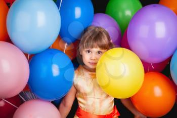Studio portrait of funny little Caucasian blond girl with colorful balloons on back background