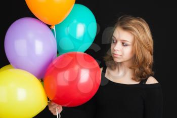 Studio portrait of teenage blond girl with colorful balloons over black background