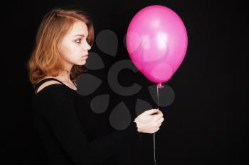 Studio profile portrait of teenage blond girl with pink balloon over black background