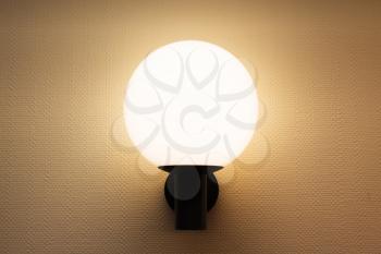 Round wall lamp illuminated white wall with textured wallpaper