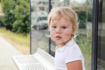Cute Caucasian blond baby girl waits on a bus stop