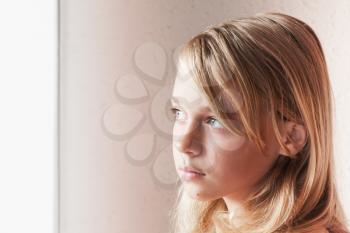 Close up portrait of beautiful blond Caucasian girl near a window with white curtains