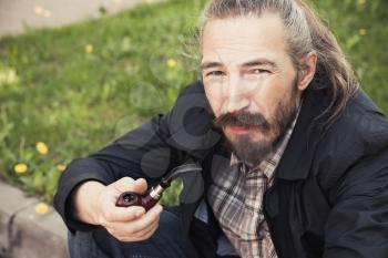 Asian man smoking a pipe on green grass in park, close-up photo with selective focus