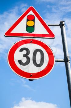 Traffic lights and speed limit 30 km per hour are on one metal post. Road signs over blue sky background