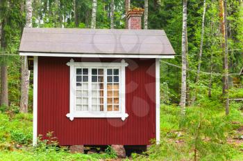 Small Scandinavian red wooden house over green forest background. Kotka, Finland