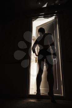 Young man standing close to opening door in dark room and looks inside to the light