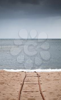 Old rusted railway goes over sandy beach on sea coast, useful for boat launching. Vertical photo with selective focus