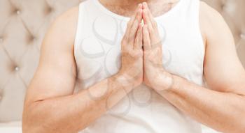 Young sad sporty Caucasian man torso in white shirt with praying hands gesture