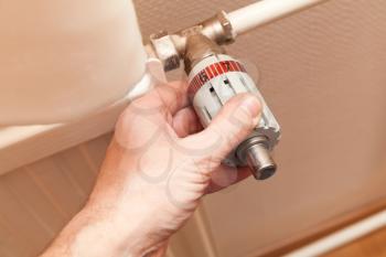 Male hand adjusts heat control on a radiator. Modern house heating technology