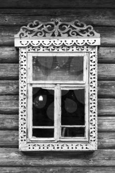 Traditional rural Russian architecture details. Window with carved wooden frame in wall made of rough logs, black and white retro style photo