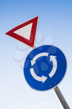 Triangle Give way and round Traffic roundabout road signs on one metal pole over blue sky