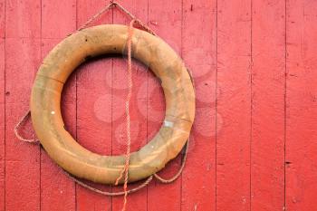 Old orange lifebuoy hanging on red wooden wall in Norway