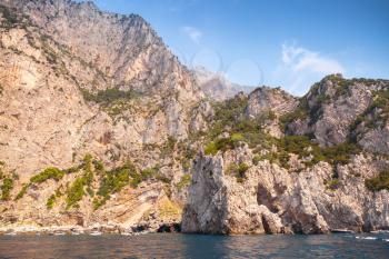 Landscape with rocky coast of Capri island, Mediterranean Sea, Italy. Small pleasure boat enters coastal cave 