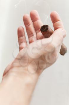 Handmade cigar in male hand, close up photo with selective focus over white wall background 