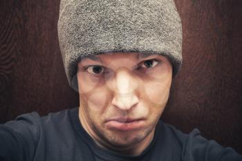 Young agressive Caucasian man in gray hat. Close-up studio face portrait over dark wooden wall background, selective focus