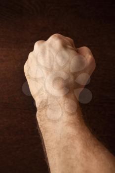 Strong male fist over dark wooden wall background