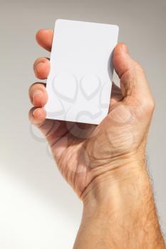 Male hand holds white empty card over gray wall background, close up photo with selective focus