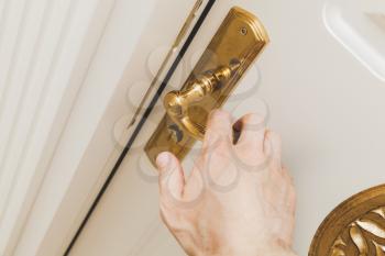 Male hand opens white wooden door with golden handle, close up photo with selective focus