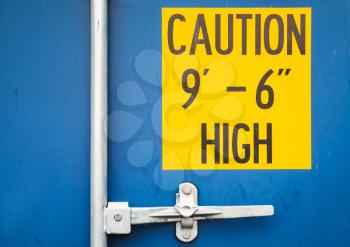 Caution high yellow sign on closed gate of standard blue cargo shipping container