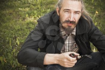 Young asian bearded man smoking pipe in summer park, closeup portrait