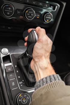 Driver hand holds gear lever of modern luxury crossover car. Close-up photo with selective focus