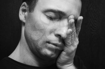 Young stressed Caucasian man with closed eyes. Studio portrait over dark wall background, black and white photo