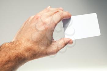 Male hand holds white empty card over gray background, close up photo