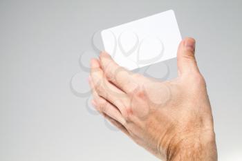 Male hand holds white empty card over gray background, close up photo, selective focus
