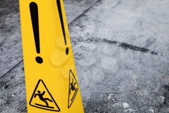 Caution wet floor, yellow warning sign stands on gray asphalt urban ground, closeup photo