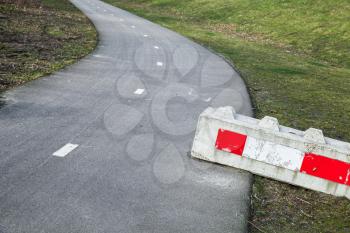 Concrete road block with red white striped warning sign lays on the roadside