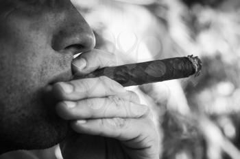 Young European man smokes big cigar, close up monochrome photo with selective focus. Dominican Republic