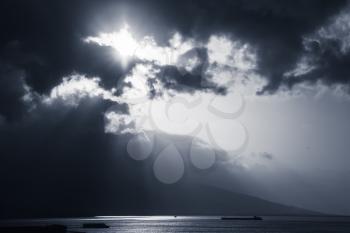 Dramatic sky with clouds and sunlight rays over sea. Blue toned photo filter effect