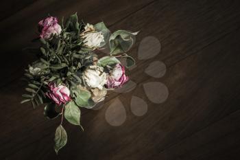 Bouquet of dried red and white roses stands on wooden table, closeup low key photo with soft selective focus. Top view