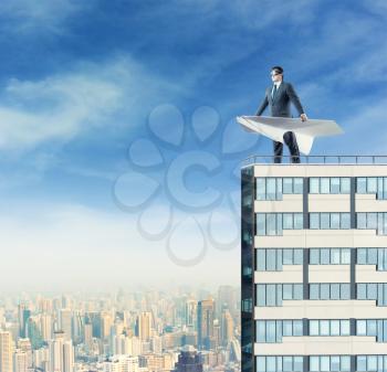 Businessman with paper airplane on the top of a high building