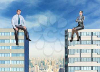 Businessman and businesswoman sit on the tops of two high buildings against the sky
