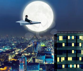 Businessman on paper airplane is flying above the city in the night