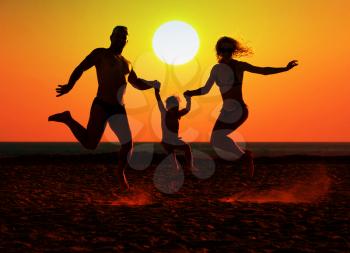 Silhouette of happy family jumping on the beach at sunset