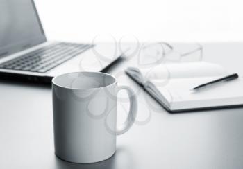 White cup, laptop, notebook and pen on the table