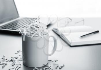 Cup full of shredded paper and laptop, notebook, pen