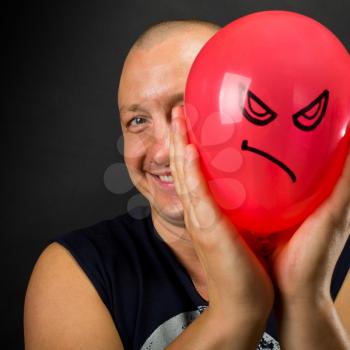 Happy man hiding behind red balloon with angry smiley