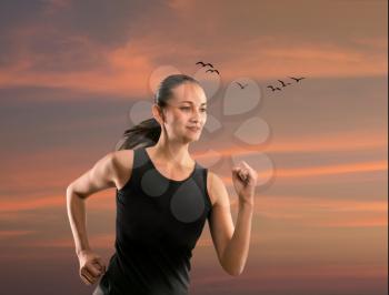 Young woman running outdoors against evening sky