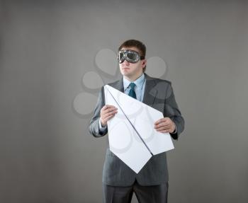 Businessman holding paper plane and wearing goggles isolated in gray