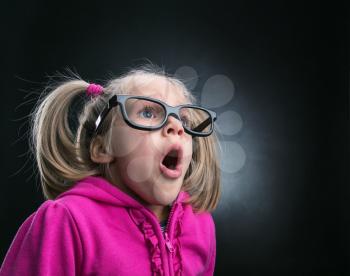 Little astonished girl in funny big spectacles on grey background