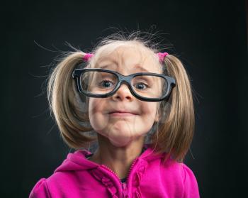 Funny little girl in big spectacles on grey