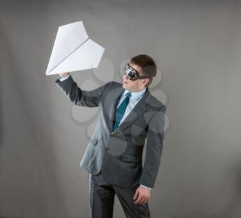 Businessman with paper plane and wearing goggles isolated in gray