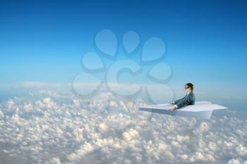 Businessman flying on big white paper plane and wearing goggles isolated on sky background