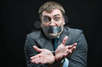Businessman with mouth and hands  covered by masking tape preventing speech, studio shoot
